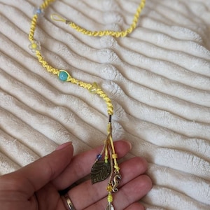 Peut inclure: Un élastique à cheveux tressé jaune avec des perles et des breloques colorées, dont une feuille, un hippocampe et une plume.