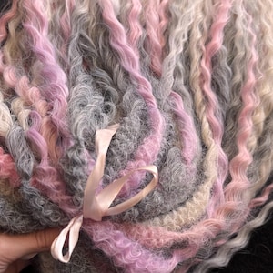 May include: A bundle of wavy, multi-colored yarn in shades of pink, gray, and white. The yarn is tied together with a pink ribbon.