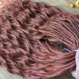May include: A set of long, wavy, auburn-colored human hair extensions with a pink elastic band.
