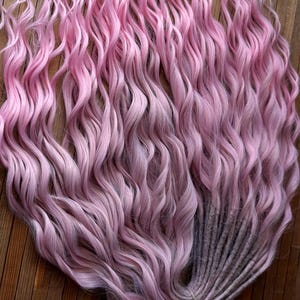 May include: A bundle of long, wavy synthetic hair extensions in a light pink ombre color. The hair is tied together with a string.