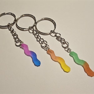 May include: Three silver keychains with colorful gummy worm charms. The charms are in shades of blue, yellow, and green.