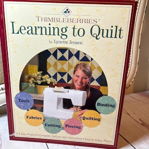 May include: A book titled "Learning to Quilt" by Lynette Jensen. The cover features a woman using a sewing machine, with colorful circles labeled "Tools," "Fabrics," "Cutting," "Piecing," "Quilting," and "Binding."