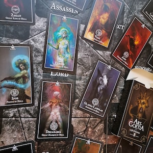 May include: A set of tarot cards featuring illustrations of demons and their titles. The cards are black with gold accents and feature a variety of demon imagery, including a demon with horns and a crown, a demon with wings and a sword, and a demon with a skull and crossbones. The cards are arranged in a random order on a dark surface.