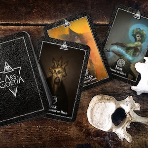 May include: A black leather-bound box with the text "ARS GOETIA" on the front.  There are four cards on a wooden surface, each with a different image and text.  The cards are from a deck of tarot cards.  The cards are: "LILIAL, Duke of Hell", "IPOS, Prince of Hell", "BUER, President of Hell", and "Astarte, Countess of Hell".