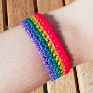 May include: A rainbow coloured crocheted bracelet on a person's wrist.
