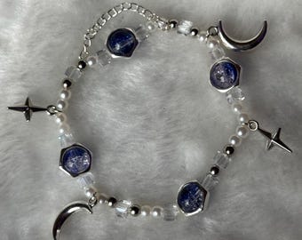 May include: A celestial-themed bracelet featuring a mix of white faux pearls, clear faceted beads, and silver-toned accents. The bracelet includes blue-toned hexagonal beads, crescent moon charms, and star charms. The bracelet is designed to be worn around the wrist.