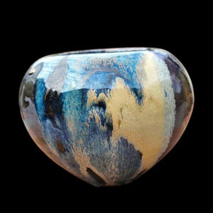 May include: A heart-shaped ceramic vase with a blue, gold, and black glaze. The vase has a unique, abstract design.