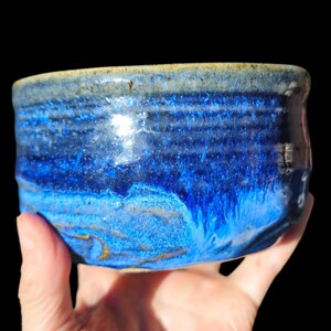 Puede incluir: Un cuenco de cerámica hecho a mano con un vibrante esmalte azul. El cuenco presenta una superficie texturizada con líneas horizontales y un acabado brillante. El color pasa de un índigo profundo a un tono más claro, casi turquesa.
