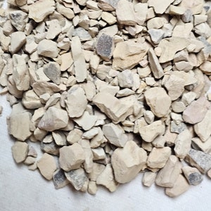 May include: A pile of small, light brown, irregularly shaped rocks. The rocks are on a white surface.