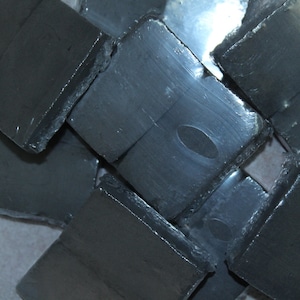May include: A close-up of several rectangular pieces of dark gray graphite, stacked on top of each other.