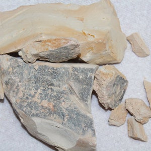 May include: A collection of broken pieces of clay in various shades of brown, beige, and gray. The clay is rough and textured, with some pieces showing signs of weathering.