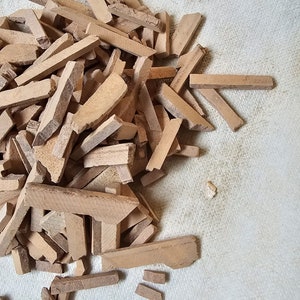 May include: A pile of broken brown wooden craft sticks. The sticks are various lengths and widths. The sticks are on a white surface.