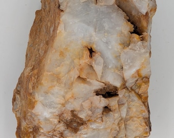 May include: A rough-hewn quartz specimen with a mix of white, tan, and brown hues. The rock has a crystalline structure with visible fractures and variations in color. The surface is uneven, showcasing the natural texture of the stone.