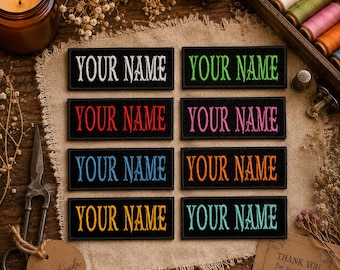 May include: Eight black embroidered patches with the text "YOUR NAME" in various colors: white, green, red, pink, blue, orange, yellow, and teal. The patches are displayed on a tan fabric surface.