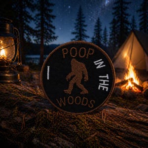 May include: A black circular patch with the text "POOP IN THE WOODS" and a brown Bigfoot silhouette. The patch is embroidered with white and brown thread. The background shows a campfire, tent, and starry night sky.