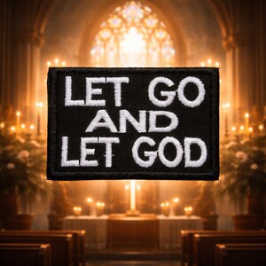 May include: A black rectangular patch featuring the white embroidered words "LET GO AND LET GOD". The background is a blurred church interior with candles and a stained glass window.