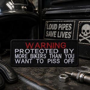 以下が含まれることがあります： 白と赤で「WARNING PROTECTED BY MORE BIKERS THAN YOU WANT TO PISS OFF」の文字が刺繍された黒いパッチ。パッチは、黒いバイクのヘルメット、手袋、工具を背景にした、質感のある表面にあります。