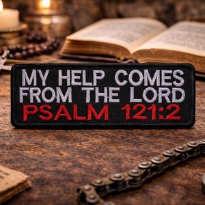 May include: Black patch with white embroidered text reading "MY HELP COMES FROM THE LORD" and red text "PSALM 121:2". The patch is on a wooden surface with a book, candles, and a cross in the background.