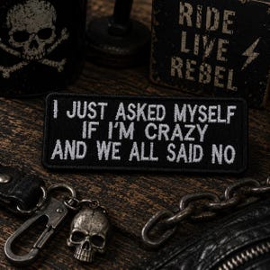 May include: A black embroidered patch with the text "I JUST ASKED MYSELF IF I'M CRAZY AND WE ALL SAID NO." The image also includes a skull keychain, a metal chain, and a sign that says "RIDE LIVE REBEL."
