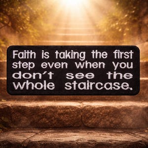 May include: A black rectangular patch with white embroidered text that reads: "Faith is taking the first step even when you don't see the whole staircase." The patch is set against a background of stone steps leading upwards.