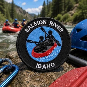 Può includere: Una toppa rotonda con le parole "Salmon River Idaho" in lettere bianche. La toppa presenta uno sfondo blu con una canoa rossa e due figure che remano. La toppa è nera con un moschettone blu e una pagaia rossa in primo piano.
