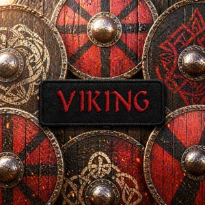 May include: A black patch with the word "VIKING" embroidered in red, set against a backdrop of weathered wooden Viking shields. The shields are round, featuring red and black designs with metal bosses.