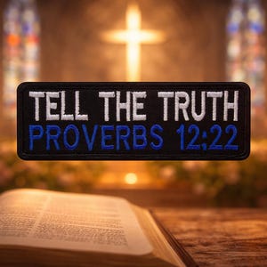 Könnte beinhalten: Ein schwarzer rechteckiger Aufnäher mit weiß gesticktem Text „TELL THE TRUTH“ über „PROVERBS 12:22“ in Blau. Der Aufnäher ist vor einem verschwommenen Hintergrund eines Kircheninneren mit Kreuz und Kerzen platziert.