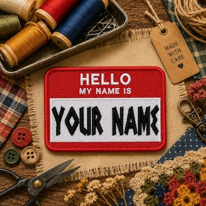 May include: A red and white embroidered patch with the text "HELLO MY NAME IS YOUR NAME" in white and black. The patch is surrounded by sewing supplies, including spools of thread, scissors, and buttons, suggesting a crafting theme.