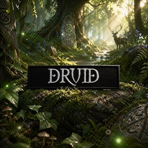 Könnte beinhalten: Ein schwarzer Aufnäher mit dem Wort "DRUID" in Weiß gestickt, vor einer moosigen Waldkulisse. Das Bild zeigt einen Hirsch, Bäume und einen Bach, wodurch eine mystische Atmosphäre entsteht. Der Aufnäher ist das zentrale Element.