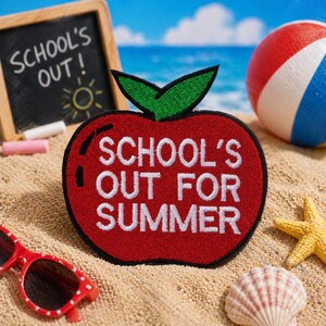 Könnte beinhalten: Ein roter, apfelförmiger Aufnäher mit dem weißen Text "SCHOOL'S OUT FOR SUMMER". Der Aufnäher befindet sich an einem Sandstrand mit einem Strandball, einer Sonnenbrille, einer Tafel, einem Seestern und einer Muschel. Auf der Tafel steht "SCHOOL'S OUT!"