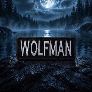 Peut inclure: Écusson rectangulaire noir avec le mot "WOLFMAN" en blanc. Le patch est placé sur un fond sombre et texturé, avec un paysage de lac et de forêt éclairés par la lune.