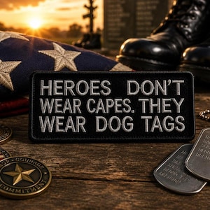May include: A black patch with the text "HEROES DON'T WEAR CAPES. THEY WEAR DOG TAGS" is displayed. The image also includes an American flag, military dog tags, coins, and black combat boots, all on a wooden surface.