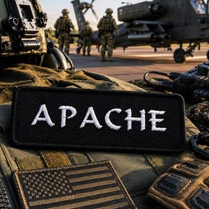 May include: An assortment of military gear, including a black patch with the word "APACHE" embroidered in white, an American flag patch, and a military helicopter in the background. The scene suggests a military theme.