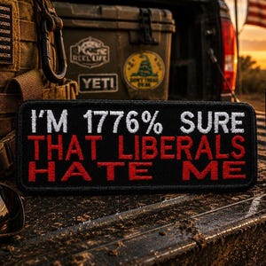 May include: Black embroidered patch with the text "I'M 1776% SURE THAT LIBERALS HATE ME" in white and red. The patch is on a textured surface with sunglasses and a tumbler with an American flag design.