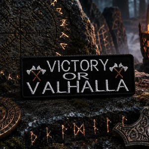 May include: Black patch with white embroidered text "VICTORY OR VALHALLA" and crossed axes. The patch is set on a textured stone surface with Viking symbols and a fire in the background. The patch is rectangular.