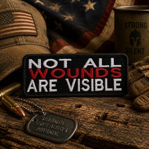 Può includere: Una toppa nera con la scritta "NOT ALL WOUNDS ARE VISIBLE" in lettere bianche e rosse. La toppa è su una superficie di legno, con un berretto in stile militare, una bandiera americana e un'etichetta per cani che recita "STRENGTH ISN'T ALWAYS PHYSICAL."