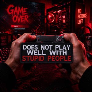 May include: A black patch with white text that reads "DOES NOT PLAY WELL WITH STUPID PEOPLE" in a gaming setup. The background includes a game console controller, a computer screen displaying "GAME OVER", and a "NO PATIENCE LEFT" sign.