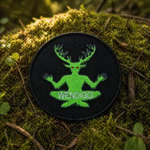 May include: A round black patch featuring a green Wendigo design. The Wendigo figure has antlers, red eyes, and is in a seated yoga pose. The word "WENDIGO" is written in white below the figure. The patch is set against a mossy background.