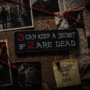 Può includere: Una toppa nera con la scritta "3 CAN KEEP A SECRET IF 2 ARE DEAD" in lettere bianche e rosse. La toppa è su una bacheca con foto, spago rosso e un biglietto con scritto "trust no one".
