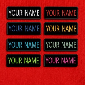 May include: Rectangular black patches with the text "YOUR NAME" embroidered in various colors: white, red, blue, yellow, green, and pink. The patches are displayed on a red background.