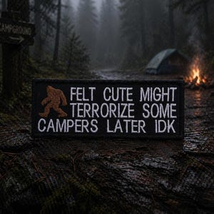 May include: Black rectangular patch with white embroidered text and a brown Bigfoot silhouette. The text reads "FELT CUTE MIGHT TERRORIZE SOME CAMPERS LATER IDK". The patch is set against a forest backdrop with a campsite and campfire.