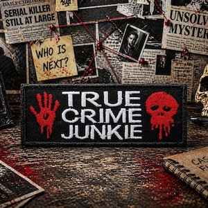 May include: A black patch with the words "TRUE CRIME JUNKIE" in white. A red hand and a red skull with dripping blood are on either side of the text. The patch is on a wooden surface with crime scene elements.