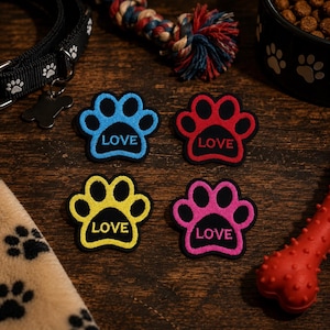 May include: Four colorful paw-shaped patches with the word "LOVE" embroidered on them. The patches are blue, red, yellow, and pink, with black outlines. Other dog-related items, such as a collar, a toy, and a food bowl, are also visible.