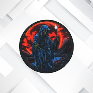 Op de afbeelding: Een ronde geborduurde patch met een gekapte figuur in een donkerblauwe robe die een fakkel vasthoudt. De figuur staat tegen een achtergrond van een rode maan en een donker, rotsachtig landschap.