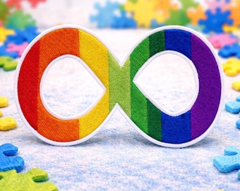 Puede incluir: Un parche bordado con el símbolo del infinito en colores del arcoíris, con un borde blanco, es el elemento central. La imagen está salpicada de coloridas piezas de rompecabezas. El fondo es azul claro, creando una imagen brillante y simbólica.