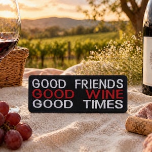 May include: A picnic scene with a glass of red wine, a bottle of Pinot Noir, and a patch that reads "GOOD FRIENDS GOOD WINE GOOD TIMES." Grapes and a cork are also present, with a vineyard in the background.