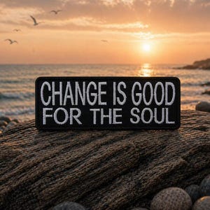 May include: A black rectangular patch with white embroidered text that reads "CHANGE IS GOOD FOR THE SOUL." The patch is set against a rocky surface with a sunset and ocean background.