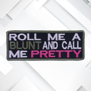 Op de afbeelding: Een zwarte geborduurde patch met groene en witte tekst die "Roll me a blunt and call me pretty" zegt met het woord "pretty" in roze.