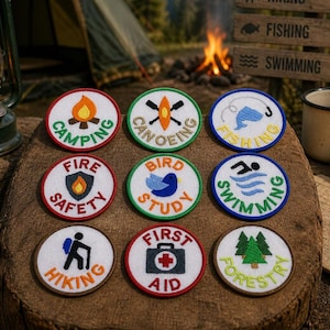 May include: Nine embroidered patches with outdoor activity themes are displayed on a wooden surface. The patches feature designs like a campfire, canoe, fish, and text such as "Camping," "Fishing," and "Hiking." The patches are round with colorful borders.