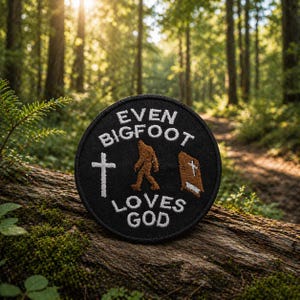 Puede incluir: Un parche negro y circular con texto e imágenes bordadas en blanco. El texto dice "EVEN BIGFOOT LOVES GOD". El parche presenta una cruz blanca, una figura de Bigfoot marrón y un libro marrón con una cruz blanca. El parche está sobre un fondo de bosque.